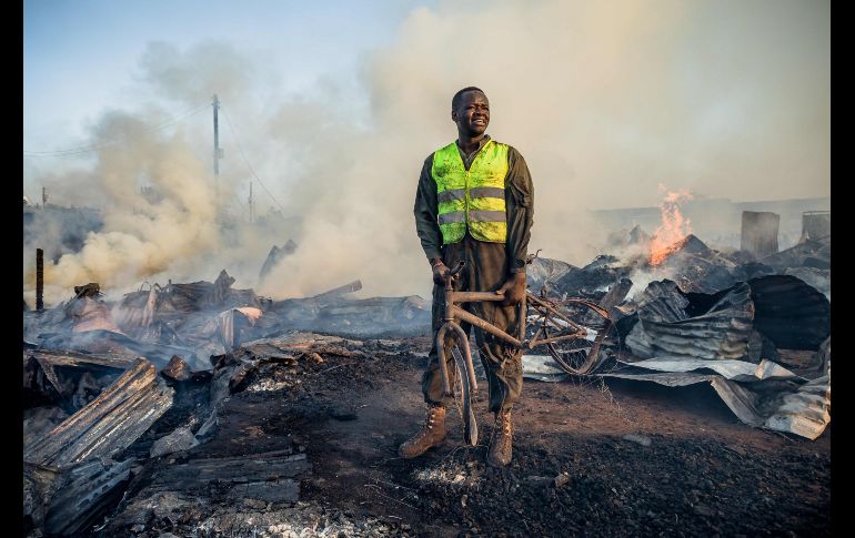 Un ciudadano que ayuda a bomberos sostiene los restos de una bicicleta tras un incendio en un mercado de ropa de segunda mano en Nairobi, Kenia. AFP/B. Otieno