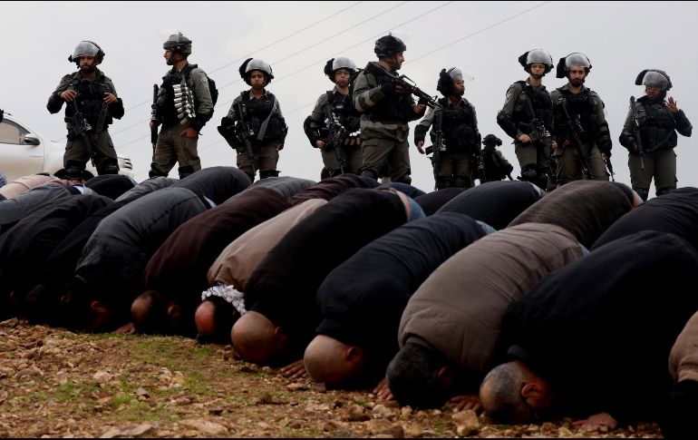 Varios soldados israelíes contemplan a un grupo de palestinos que rezan durante una protesta en la ciudad cisjordana de Tubas. EFE/A. Badarneh