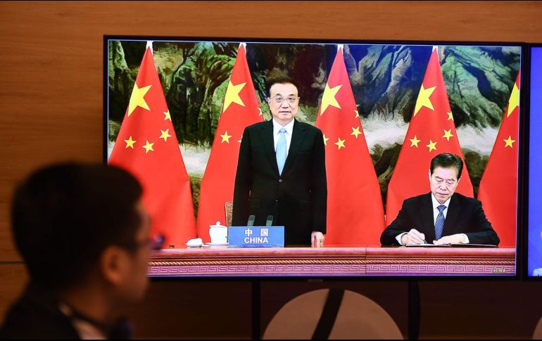 El primer ministro chino, Li Keqiang (c), y el ministro de comercio chino, Zhong Shan (d), durante la firma de la RCEP, en la ceremonia vista en una televixión en Hanói, Vietnam. La cumbre de 15 países se realizóde forma virtual por la pandemia. AFP/N. Nguyen