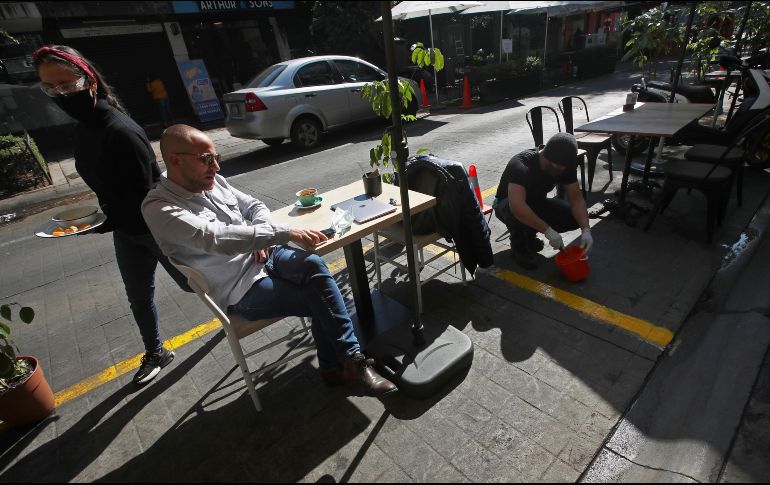 Un hombre come hoy mientras un trabajador marca una zona junto a una calle en la zona de Polanco, en Ciudad de México. AP/M. Ugarte