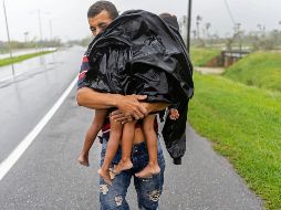 Un hombre carga a sus dos hijos, bajo la lluvia, luego de que el huracán 