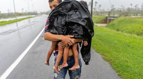 Un hombre carga a sus dos hijos, bajo la lluvia, luego de que el huracán 