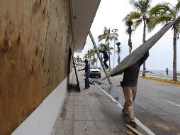 Trabajadores protegen ventanas en un edificio enfrente del mar ante la llegada de 