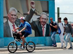 Un grupo de hombres caminan frente a una fotografía del presidente de la República de Cuba Miguel Díaz-Canel junto a Raúl Castro, en La Habana. EFE/E. Mastrascusa
