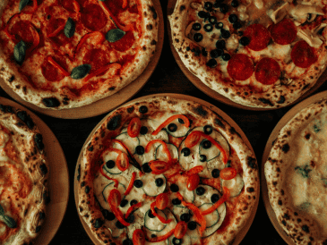 La pizza es un plato italiano, originario de Nápoles; es una base de masa de pan horneada cubierta tradicionalmente con salsa de tomate queso mozzarella y otros ingredientes. CANVA