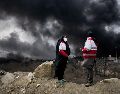 Dos mujeres de la Sociedad de la Media Luna Roja iraní permanecen de pie mientras una densa columna de humo proveniente de un ataque estadounidense-israelí contra una instalación de almacenamiento de petróleo en Teherán, Irán. AP/V. Salemi