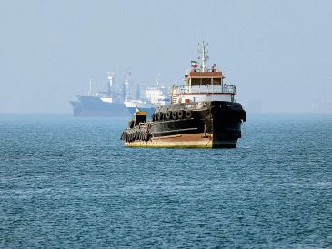 Remolcador iraní navega cerca de un buque anclado en el Estrecho de Ormuz, frente a Bandar Abbas; Teherán niega paso de barcos comerciales. AFP