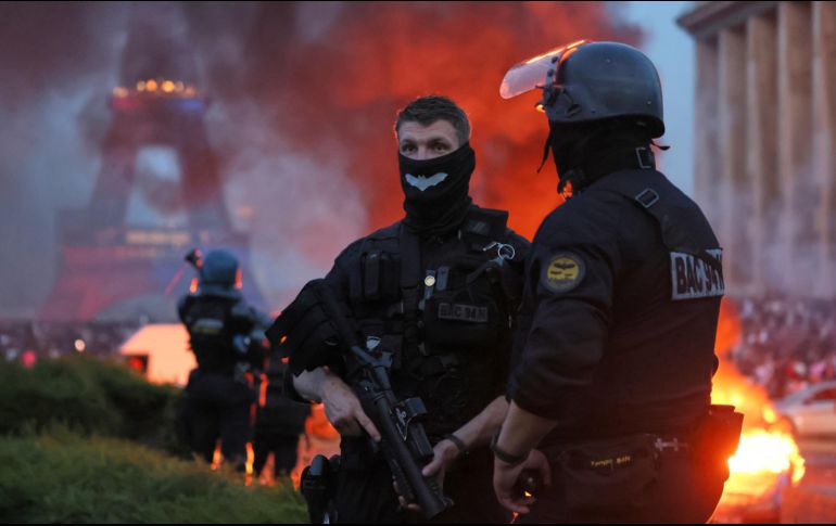 Un automóvil arde y estallan fuegos artificiales mientras la policía observa a los aficionados del PSG celebrar en París. AP/T. Padilla