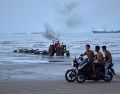 Jóvenes a bordo de motocicletas a lo largo de la orilla mientras un tractor saca equipo del agua y al fondo se pueden ver buques mercantes aparentemente anclados en el estrecho de Ormuz. AP/R. Poudat