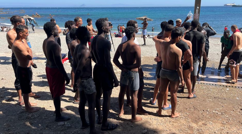 Jóvenes inmigrantes que duermen en la calle hacen fila para bañarse en la playa del Trampolín, tras acceder a Ceuta el pasado jueves. EFE/Reudan
